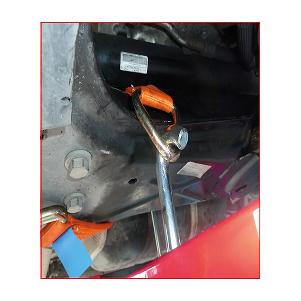 Nahaufnahme von Werkzeug unter einem Auto. Ein Hebezeug mit orangefarbenen Gurten ist befestigt, daneben ein Schraubenschlüssel.